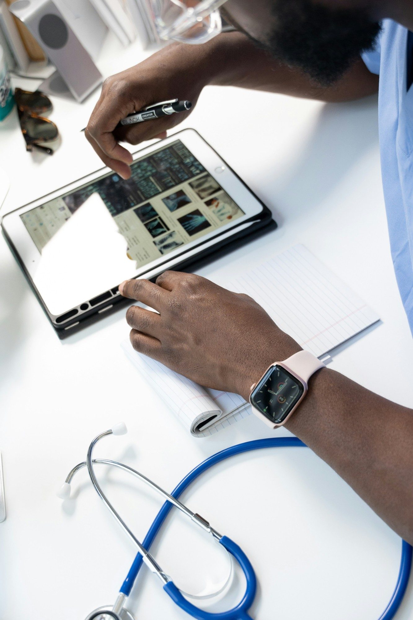 A clinician in scrubs reviews imaging on a tablet at a desk, a notepad and stethoscope beside them.