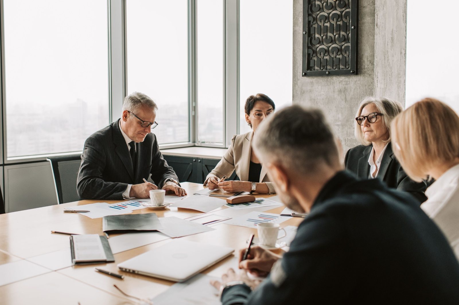 Executives review printed reports around a boardroom table in a high-floor office.